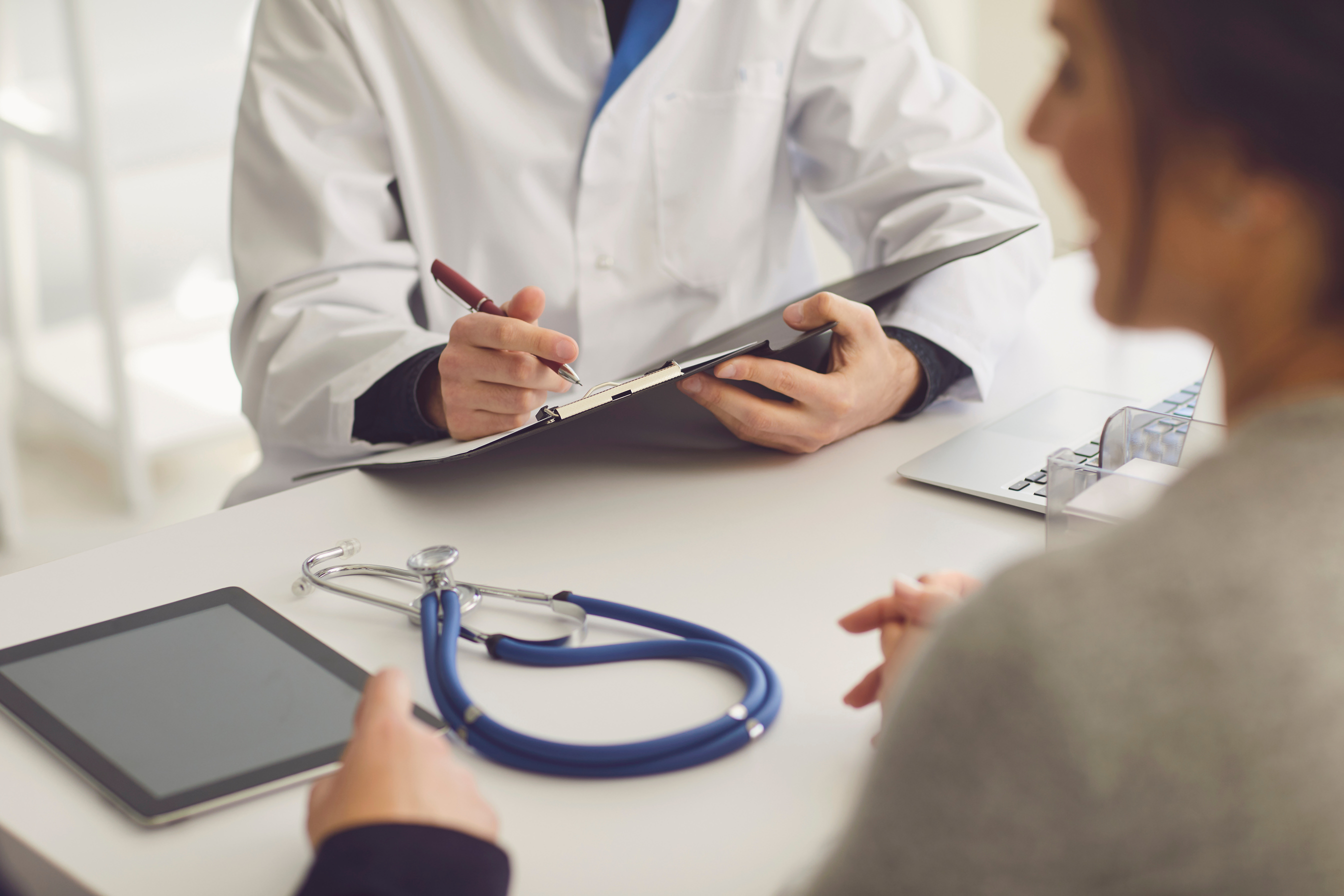 Confident Doctor and Couple Patient Sitting at the Table in Clinic Office. Family Doctor. Faceless.